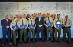 Williamson County Sheriff’s Office deputies, command staff members stand together at the Tennessee Law Enforcement Training Academy graduation. Several deputies in uniform hold blue TLETA certificate folders, with signed graduation boards displayed on the wall behind them.
