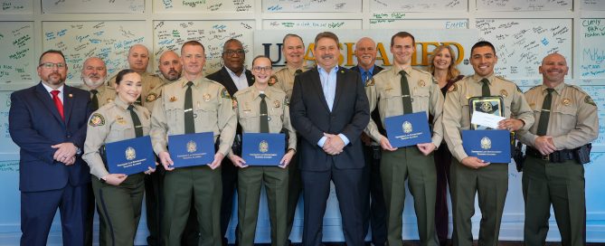 Williamson County Sheriff’s Office deputies, command staff members stand together at the Tennessee Law Enforcement Training Academy graduation. Several deputies in uniform hold blue TLETA certificate folders, with signed graduation boards displayed on the wall behind them.