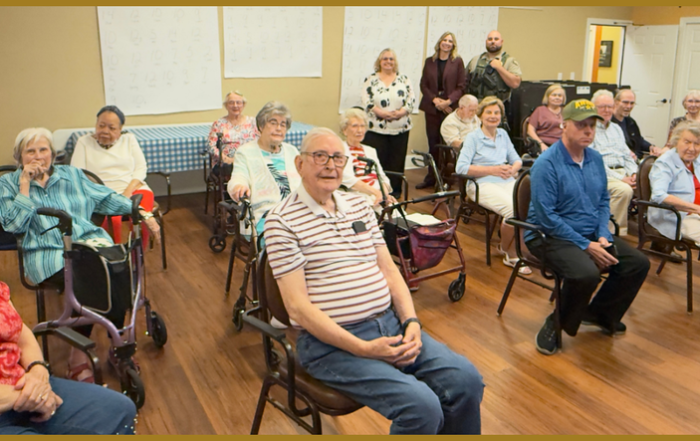 A group of senior residents sits in a community room during a public safety presentation. Three Members of the Williamson County Sheriff’s Office stand at the back of the room while attendees face the camera.