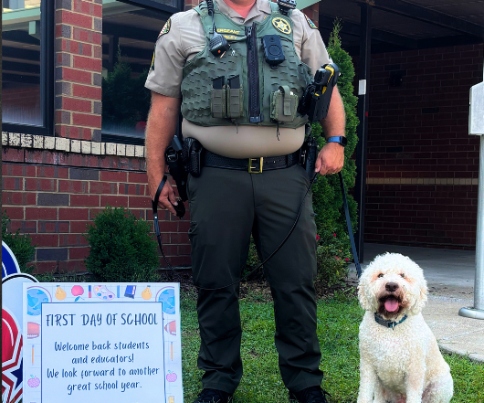 Sergeant Morley and K9 Bolo pose for a first day of school photo at campus. K9 Bolo, a police dog assigned to school duty, sits beside Sergeant Morley as they help welcome students back for the new school year.