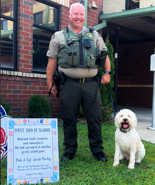 Sergeant Morley and K9 Bolo pose for a first day of school photo at campus. K9 Bolo, a police dog assigned to school duty, sits beside Sergeant Morley as they help welcome students back for the new school year.