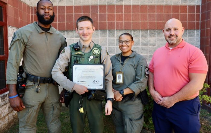 Deputy Harper stands with three colleagues outside the Williamson County Sheriff’s Office detention facility, holding a framed Certificate of Appreciation recognizing him as the September Employee of the Month.
