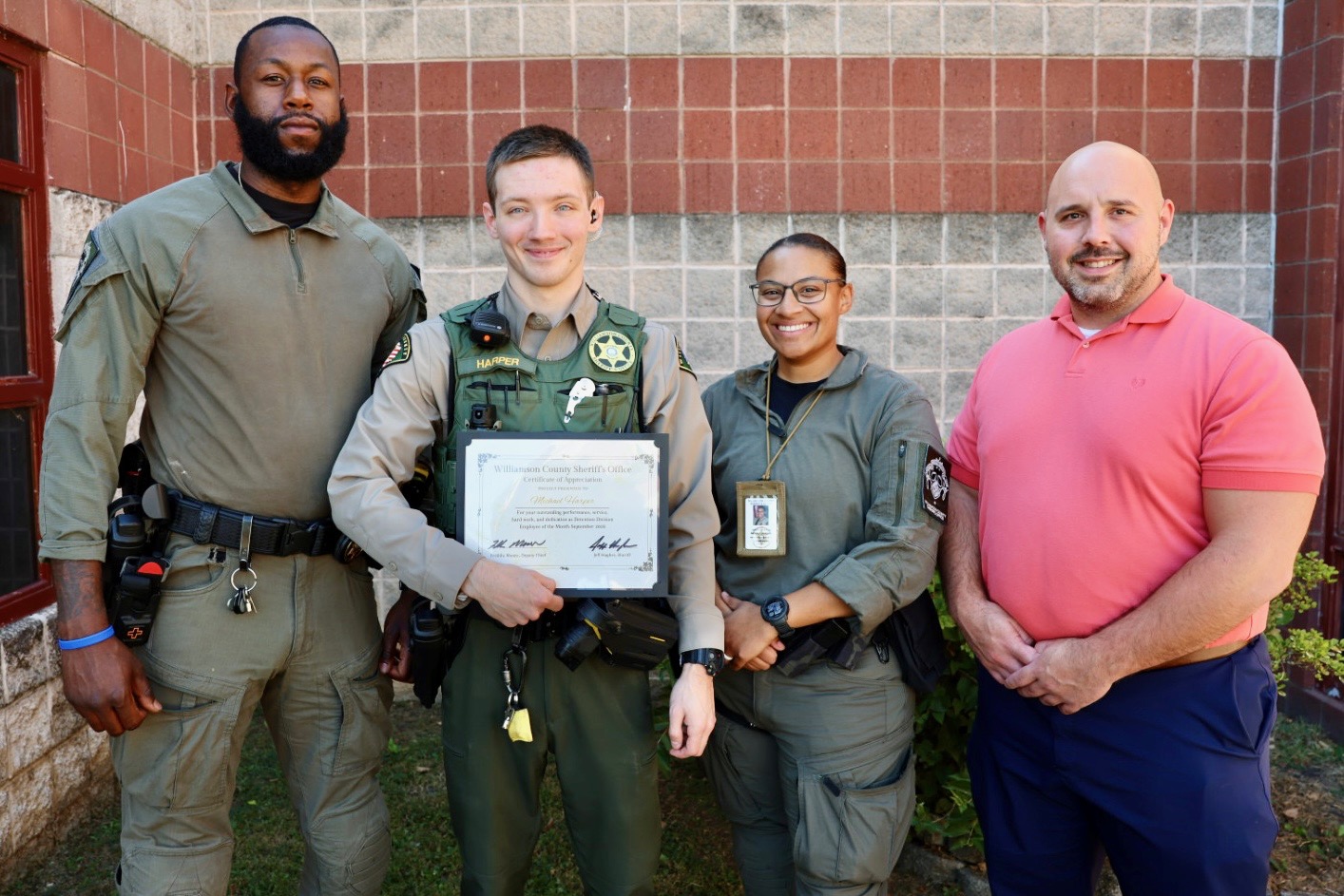 Deputy Harper stands with three colleagues outside the Williamson County Sheriff’s Office detention facility, holding a framed Certificate of Appreciation recognizing him as the September Employee of the Month.