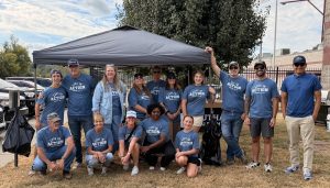 A group of Southall Church volunteers pose together outdoors beneath a canopy during a Deputy Appreciation Cookout. Many are wearing matching blue “Love in Action” shirts, with food and grilling equipment set up behind them.
